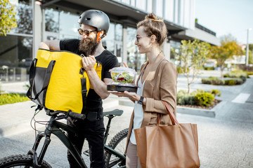 Courier delivering fresh lunches to a young business woman on a bicycle with thermal backpack....