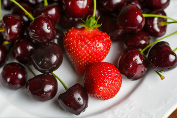 Glossy cherries on a white plate with red strawberries. Ripe and juicy cherry fruits and strawberries