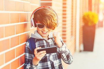 Happy smiling boy with smartphone playing game outside, over brick wall. New generation, leisure,...