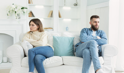 Young couple sitting on different sides of couch after quarrel - obrazy, fototapety, plakaty