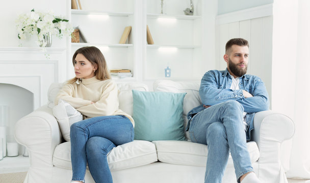 Young couple sitting on different sides of couch after quarrel
