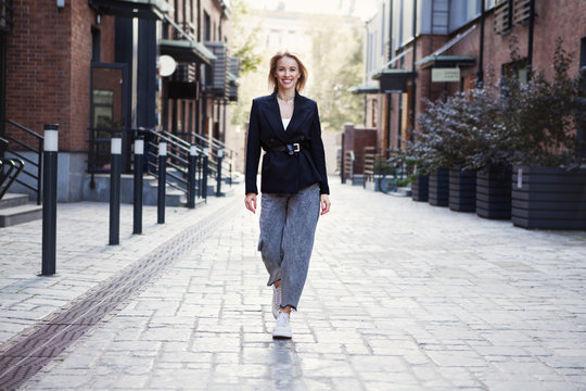 Confident Businesswoman In Stylish Office Clothes walking city street. . Beautiful Smiling Woman Going To Work, Wearing Fashionable Spring or fall black jacket, oversize slouchy jeans