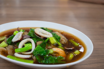 Fried noodle with pork ,Kale Seafood, shrimp, squid in cup on wooden table.Thai food