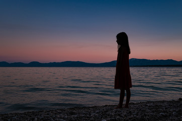 Fototapeta premium Silhouetter of a young girl standing on a beach looking on horizon after sunset