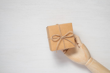 Wooden mannequin hand opens a gift in a box tied with twine. Gift background concept for holiday makers. Greeting card for christmas, birthday and new year.