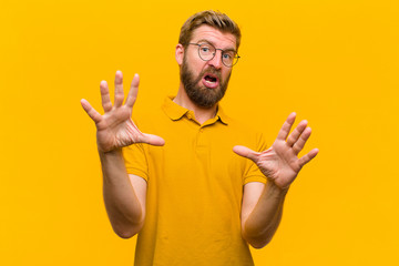 young blonde man feeling terrified, backing off and screaming in horror and panic, reacting to a...