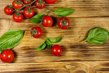 Fresh cherry tomatoes with green basil leaves on a wooden table. Top view