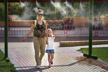 Young mother with her daughter in hot weather, cool off at the gates of climate control in the...