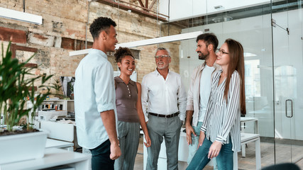 Happy and successful. Group of cheerful business people standing in the modern office, smiling and...