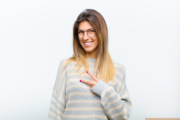young pretty woman feeling happy, positive and successful, with hand making v shape over chest,...