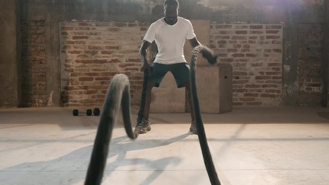 Sport man doing battle ropes exercise workout at gym