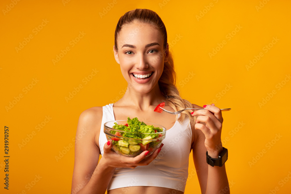 Wall mural Fitness Girl Eating Vegetable Salad Standing Over Yellow Background