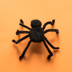 Black spider on orange background. View from above. Minimal Halloween party decor.