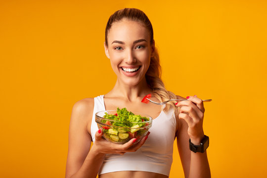 Fitness Girl Eating Vegetable Salad Standing Over Yellow Background