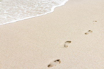Beach, wave and footprints in cloudy day. Vacation concept.