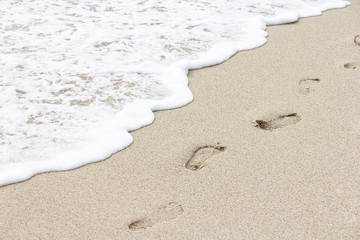 Beach, wave and footprints in cloudy day. Vacation concept.