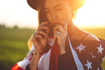 Boho chic woman in hat with american flag wearing silver rings with turquoise stone plays on harmonica at sunset. Jewerly indie girl with hippie style and boho fashion. Travel to america
