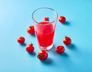 Glass of juice and tomatoes on a blue background
