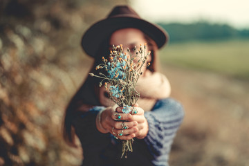 Autumn brunette woman in a brown hat and in a knitted clothes wearing silver rings with turquoise stone holds bouquet of wildflowers in hands in autumn forest outdoors in fall. Cornflowers close-up