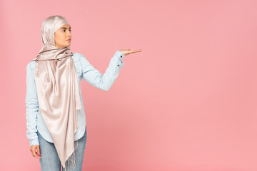 beautiful muslim woman in hijab showing something, isolated on pink