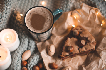 Mug of coffee with chocolate charlotte pie and nuts with burning candles in bed over lights closeup. Autumn season. Good morning. Breakfast. Still life.
