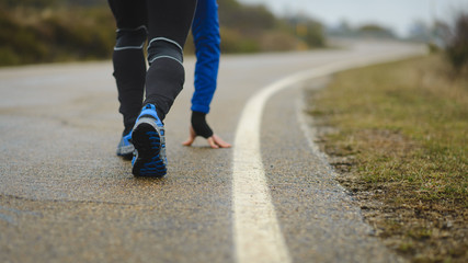 Detail of athlete legs ready for sprinting and running on asphalt road in winter.