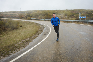 Athlete running under the snow on winter mountain road. Cold season outdoor training.