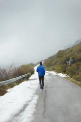 Back view of athlete running under the snow on winter mountain road.