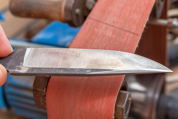 Grinding polishing sharpening knife blade on the belt grinder sander equipment. Knife making.