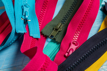 Pack lot of colorful plastic and metal zippers stripes with sliders pattern for handmade sewing tailoring on the blue painted wooden background close up selective focus © vitalis83