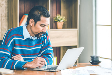 Arab businessman in casual clothes  working in the office with laptop, paper, note and a cup of coffee on working table.
