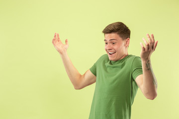 Caucasian young man's half-length portrait on green studio background. Beautiful male model in shirt. Concept of human emotions, facial expression, sales, ad. Astonished, shocked, wondered.