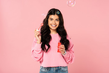pretty smiling girl playing with soap bubbles isolated on pink