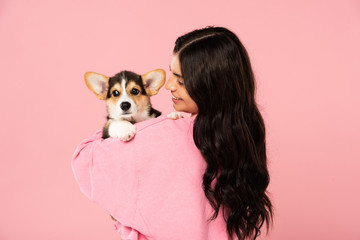 happy young woman holding Welsh Corgi puppy, isolated on pink