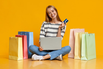 Girl with laptop and credit card surrounded by paper bags