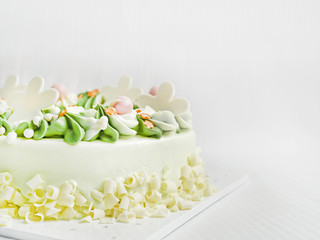 white chocolate birthday cake. is creamy, white and green, with beautiful spiral petals. On a white fabric background