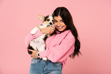 beautiful smiling girl holding Welsh Corgi puppy, isolated on pink