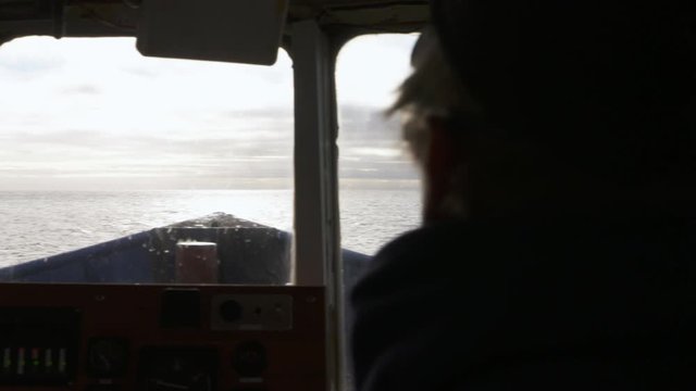 A daylight extreme closeup shot of the captain at the wheel inside the motorboat cruising the calm ocean water with the view of the wide horizon..