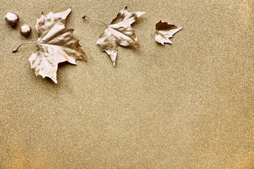 Fototapeta na wymiar Autumn flat lay with leaves painted with gold and copy-space on sparkling golden pape