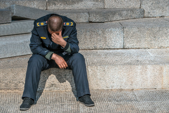 Sad policeman is sitting on the floor with his had down, he lost his job, he is alone. 