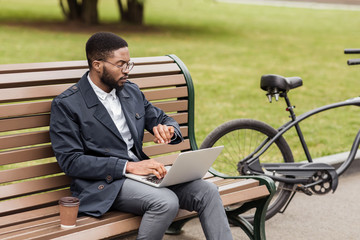 Freelance man working on laptop outdoors and checking time