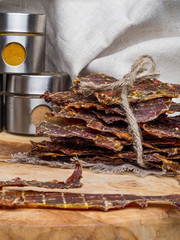 Dried or dehydrated meat slices with spices in jars, on wooden background, copy space