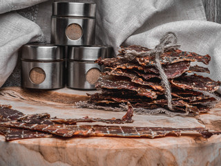 Dried or dehydrated meat slices with spices in jars, on wooden background, copy space