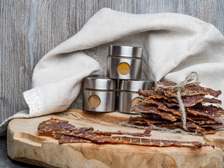Dried or dehydrated meat slices with spices in jars, on wooden background, copy space