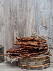 Dried or dehydrated meat slices with spices in jars, on wooden background, copy space