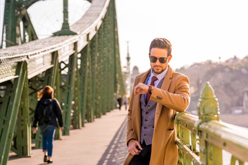 An elegant man standing on a bridge and checking the time