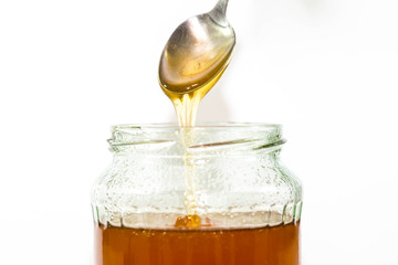 Jar filled with delicious honey, puring honey from the spoon, focus on the spoon.