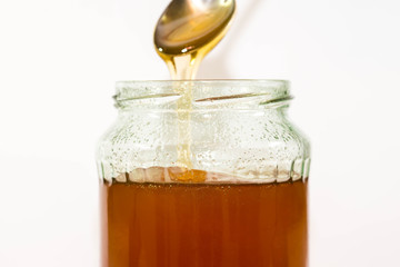 Jar filled with delicious honey, puring honey from the spoon, focus on the jar.