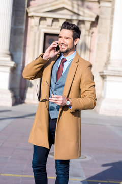 An elegant man standing on a square and talking on his phone
