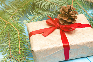 Fur spruce pine coniferous branches, gift box craft paper with red bow on the blue painted brushed wooden background